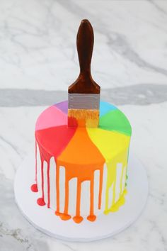 a cake with rainbow icing and a paintbrush sticking out of it's top