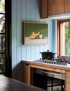 a painting hangs on the wall above an oven in a kitchen with blue walls and wooden cabinets