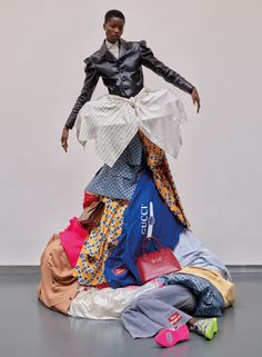 a woman standing on top of a pile of clothes in front of a white wall