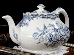 a blue and white tea pot sitting on top of a doily next to pearls