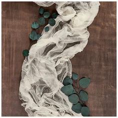 white flowers and green leaves on a wooden surface with sheer fabric over them that is covering the table