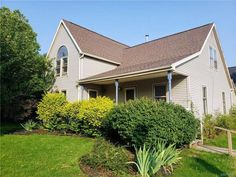 a house that is in the middle of some grass and bushes with trees around it