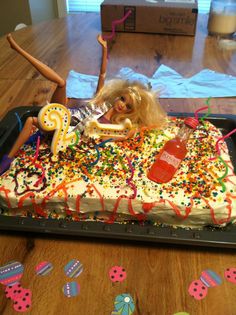 a barbie doll laying on top of a birthday cake with candles and sprinkles