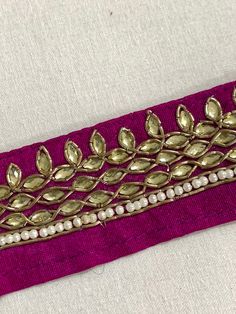 This Magenta raw silk lace trim is adorned with Light Gold rhinestones and pearls, each one delicately outlined with metallic antique gold Zardosi cords, all hand embroiderd to perfection by skilled artisans. This beautiful Magenta and antique Gold hand Embroidered Raw Silk Trims can be used for designing stylish blouses, shrugs, skirts, tunics, festive wear, wedding wear and dresses. Evening Bags, tunics, Cushions, Table cover, Shoes, Slippers, Lehengas, Christmas Décor, Outdoor Dresses, Women's formal Dresses etc. Trim width measures 3.6 centimeters (1.5 inch) wide.  Sold in 1 yard lengths. Please Note: This product is handmade and might carry certain irregularities that are part of its unique charm. The photos closely represent the colors, however some slight differences can occur due t Elegant Embroidered Border Trims For Party, Elegant Trims With Embroidered Border For Party, Elegant Party Trims With Embroidered Border, Festive Embellished Party Trims, Organic Bag, Stylish Blouses, Outdoor Dress, Raw Silk Fabric, Christmas Décor