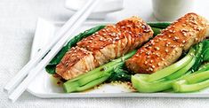 a white plate topped with meat and veggies next to chopsticks on a table