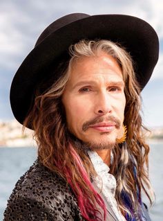 a close up of a person wearing a hat near the water with long dreadlocks