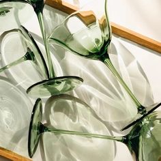 three green glasses sitting on top of a wooden tray next to each other in front of a white wall