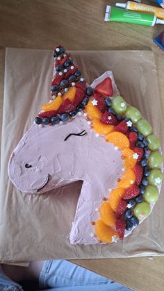 a cake shaped like a unicorn with fruit on it's face and eyes, sitting on top of a piece of brown paper