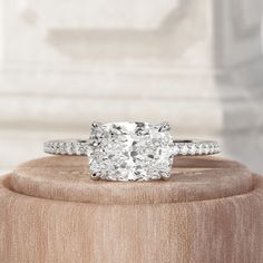 a cushion cut diamond ring on top of a wooden stand in front of a white marble wall