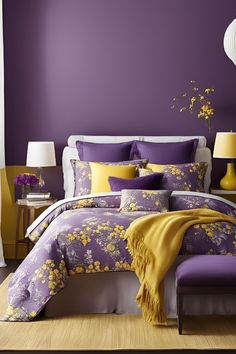 a bed with purple and yellow comforters in a bedroom next to a lamp on a table