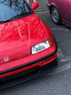 the front end of a red car parked in a parking lot next to another pink car