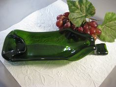 a green glass bottle sitting on top of a white table cloth next to some grapes