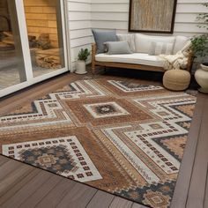 an outdoor area rug is on the wooden deck near a couch and potted plant