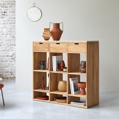 a wooden shelf with books and vases on top of it in a room next to a brick wall