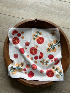 a wooden bowl with a white and red dish cloth on top of it, sitting on a wood table