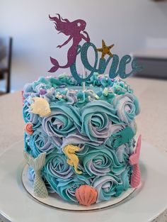 there is a cake that has blue frosting and decorations on it, with a mermaid topper