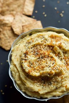 a bowl filled with hummus and crackers on top of a black table next to crackers