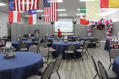 a room filled with lots of tables covered in blue cloths and american flags hanging from the ceiling