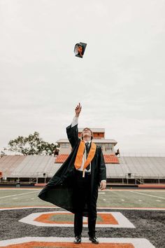 a man in a graduation gown and orange scarf flying a kite on the football field