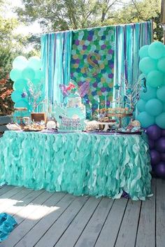 the table is set up with balloons, cake and other items for a mermaid themed birthday party