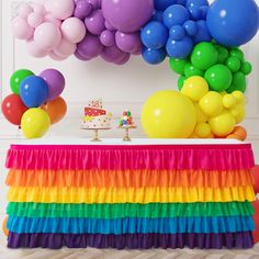 a table topped with lots of balloons and cake next to a rainbow colored skirt on top of it