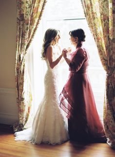 two brides standing in front of a window with their hands on each other's hips