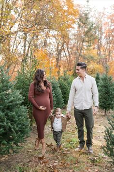 a man and woman holding hands while standing next to a baby in a christmas tree farm