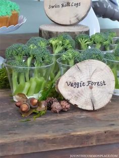 broccoli and other veggies are in plastic cups on a wooden table