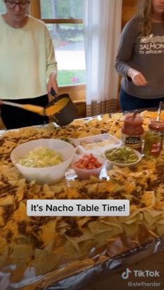 two women standing in front of a table with food on it and the caption, it's nacho table time