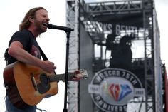 a man singing into a microphone while holding an acoustic guitar in front of a stage