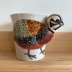 a ceramic bird sitting on top of a wooden table next to a white cup filled with berries