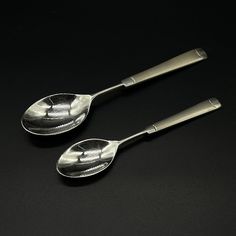 two silver spoons sitting next to each other on a black surface