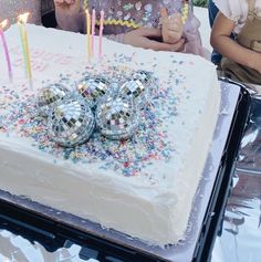 a birthday cake with candles and confetti on it, surrounded by other people