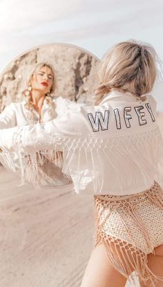 a woman in white shirt and fringe shorts standing next to a large rock with the word wife written on it