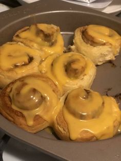 there are some rolls covered in yellow icing on the baking pan with other pastries