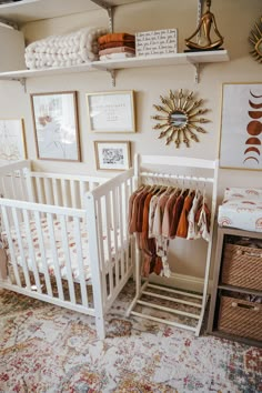 a baby's crib with clothes hanging on the wall and pictures above it