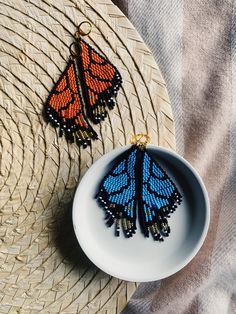 two orange and blue butterfly earrings sitting on top of a white plate next to a straw hat