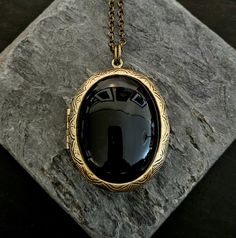 Rich black onyx framed in antiqued brass. Locket opens with 2 spaces for pictures or things. Locket hangs from long antiqued brass chain.  Details: Locket measures 45mm x35mm Locket and chain are plated brass Necklace measures 28 inches Lead and nickel free Stone is genuine onyx Please allow for possible slight color differences due to different settings on different screens. Thank you for shopping Delicate Industry :) Vintage Black Oval Pendant Jewelry, Vintage Black Brass Necklace, Vintage Black Jewelry With Antique Finish, Vintage Black Locket Jewelry, Elegant Oval Bronze Locket Necklace, Antique Black Locket Jewelry, Elegant Black Medallion Locket Necklace, Elegant Black Jewelry With Antique Finish, Handmade Oval Brass Locket Necklace