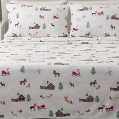 a bed covered in white sheets with reindeers and houses on them, along with christmas trees