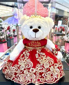 a white teddy bear wearing a red and gold dress in a store window display case