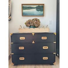 a black dresser with two baskets on top of it and a painting above the drawers