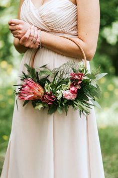 a woman in a white dress holding a brown bag with flowers and greenery on it