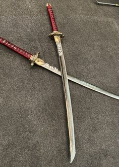 two swords are laying on the ground next to each other, one has a red handle