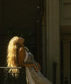 a woman with long blonde hair is sitting on a balcony looking up at the sky