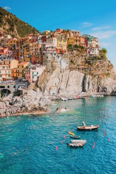 several boats floating in the blue water next to a small village on top of a hill