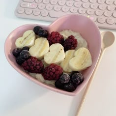 a heart shaped bowl filled with berries and bananas next to a computer keyboard on a desk