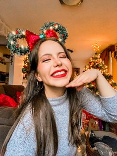 a woman with christmas wreaths on her head smiles at the camera while standing in front of a christmas tree