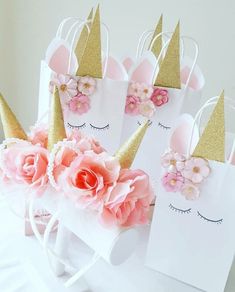 pink flowers and gold glittered unicorn ears are on top of white paper bags with floral decorations