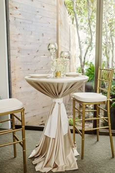 a table with two chairs and a white table cloth draped over it, in front of a window