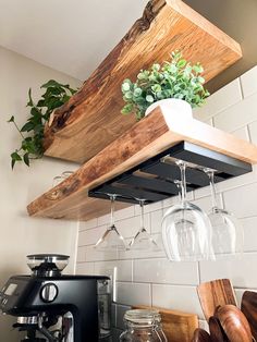 a wooden shelf with wine glasses hanging from it's sides and some plants in the middle